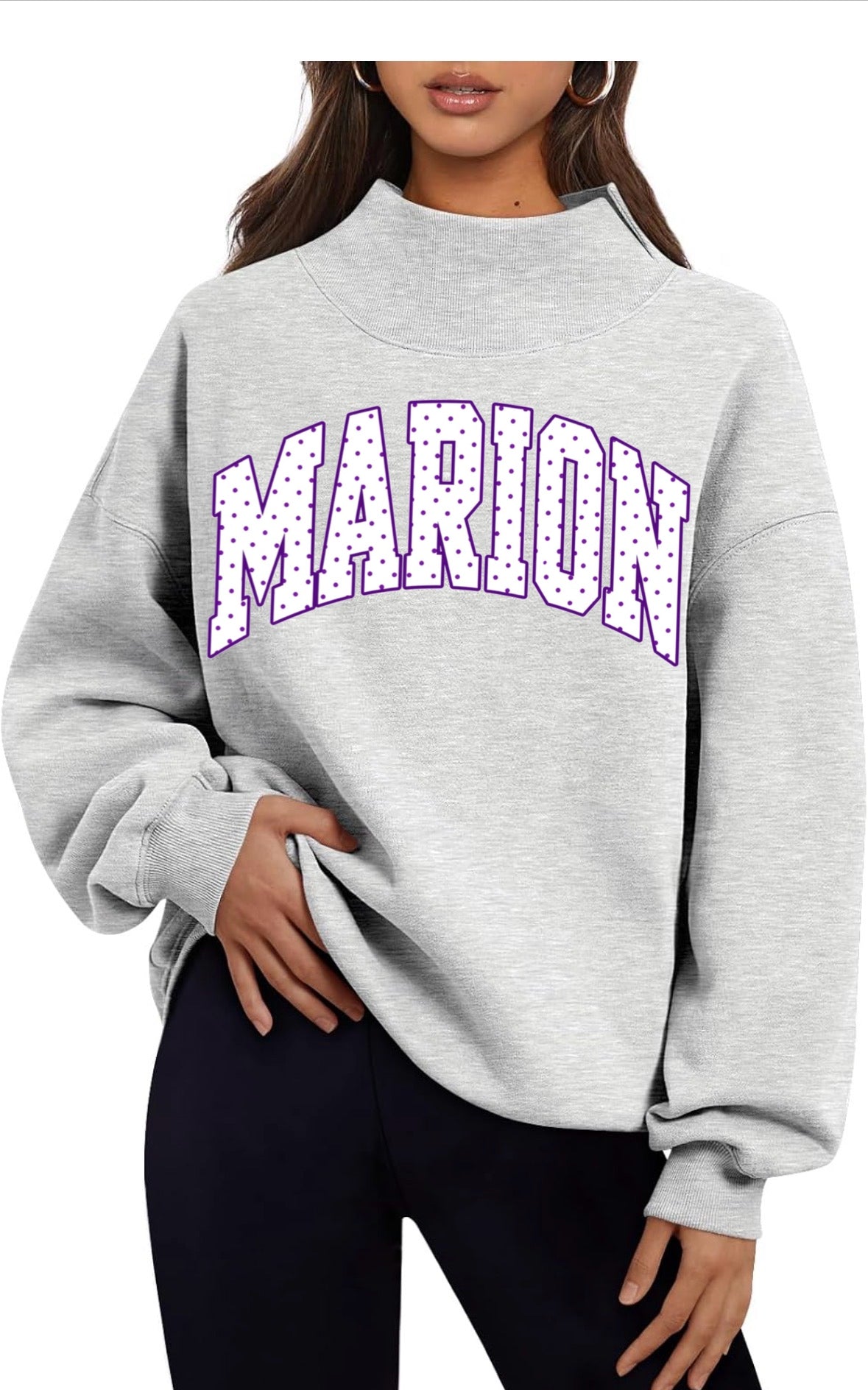 Model wearing a heather gray oversized mock neck sweatshirt with a purple and white polka dot MARION arch graphic